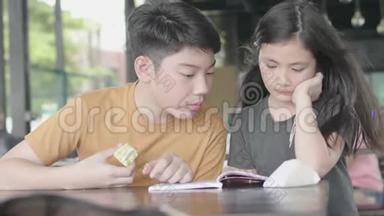 亚洲男孩和女孩用卡通书放松，可爱的亚洲孩子坐在咖啡馆里享受读书，微笑着面对